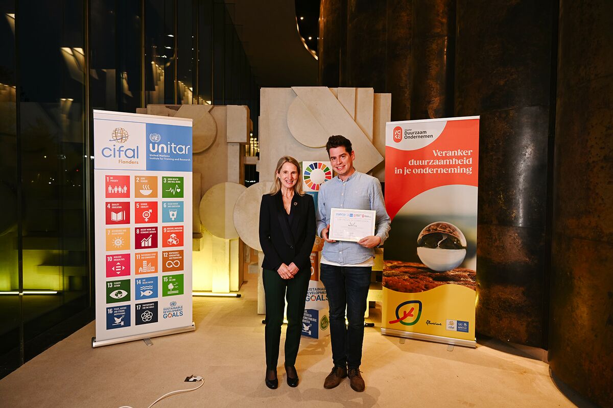 Two people posing in front of large company banners, with one person holding a certificate - reynaers