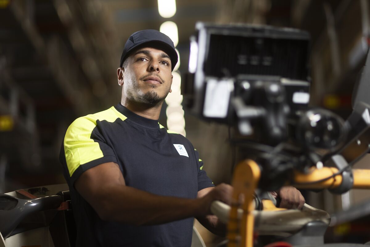 Close-up of a worker in a uniform operating machinery, with a focused expression and a blurred industrial background - Reynaers