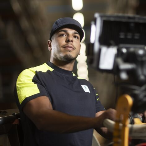 Close-up of a worker in a uniform operating machinery, with a focused expression and a blurred industrial background - Reynaers