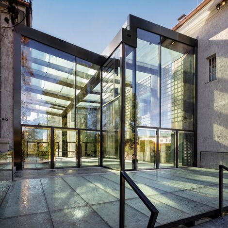 Modern glass entrance to a building with large reflective windows and sleek architectural design - Reynaers