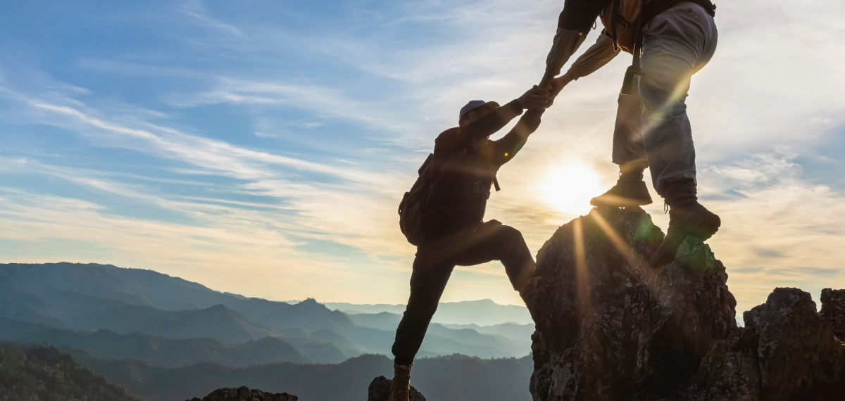 Two people climbing a mountain at sunset.